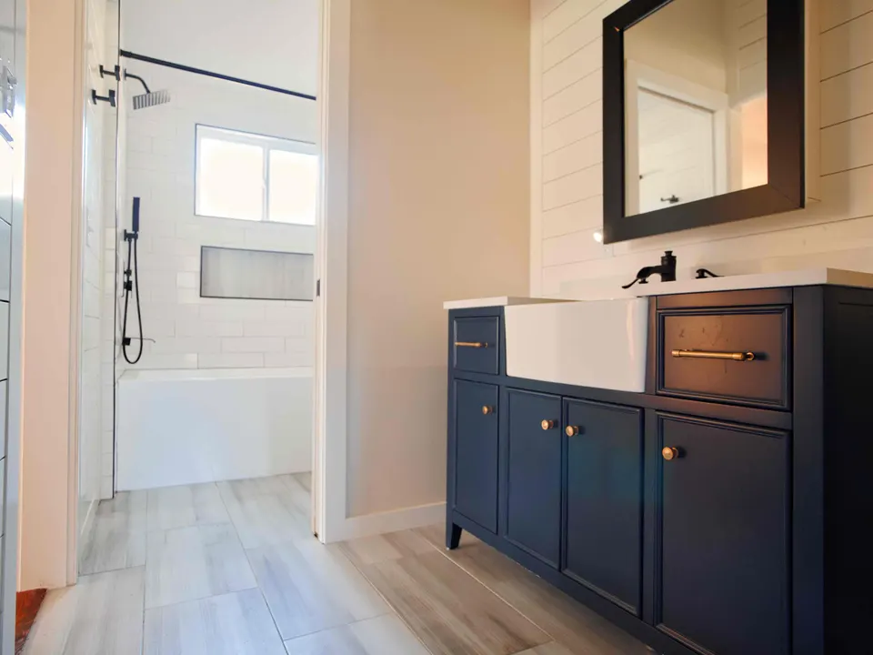 Navy vanity with a farmhouse sink and black framed mirror, with a white subway-tile tub and shower beyond