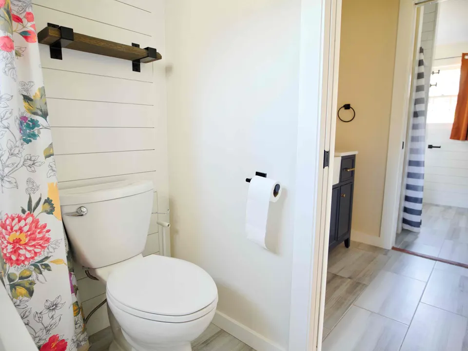 Shiplap wall with a wood shelf on black brackets, looking through to the navy vanity