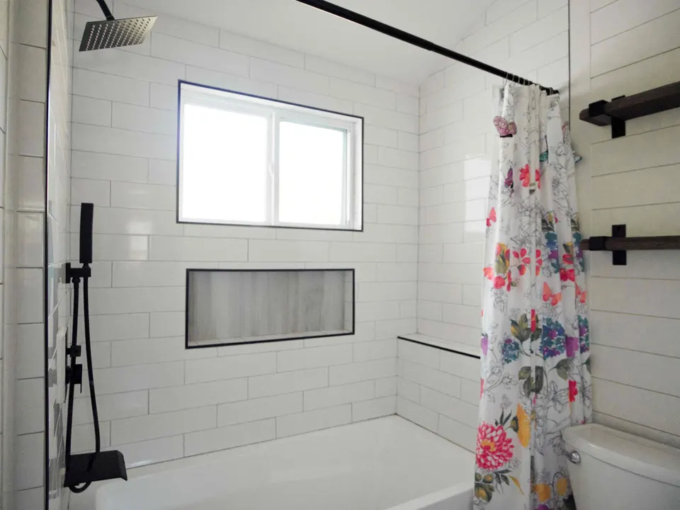 Tub and shower in large white subway tile with a long recessed niche, a window and matte black rain head