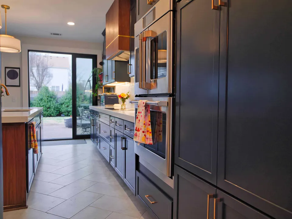 Navy cabinetry with stacked wall ovens leading to a glass door onto the patio