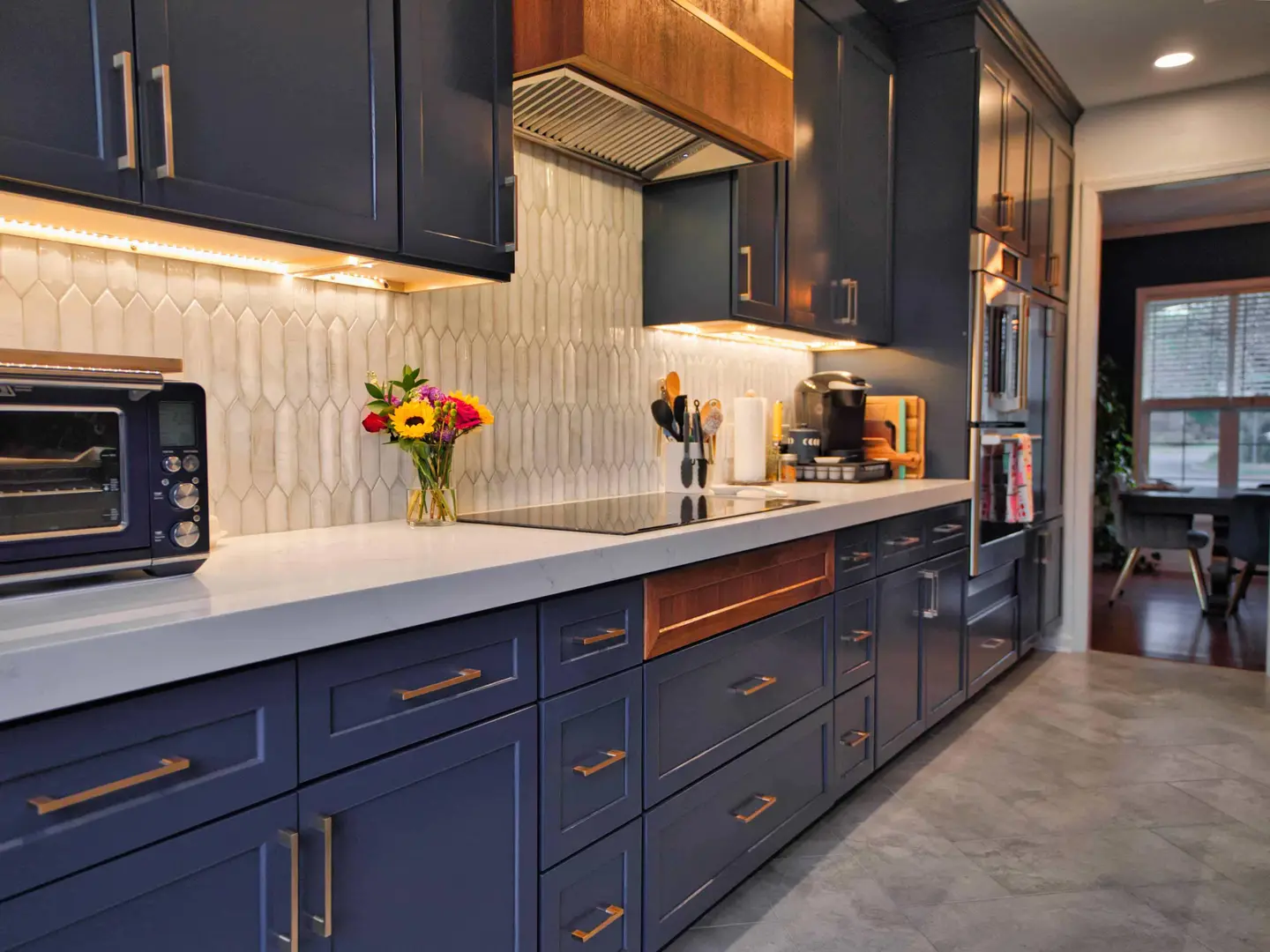 Long run of navy cabinets with a walnut accent drawer, picket tile backsplash and under-cabinet lighting