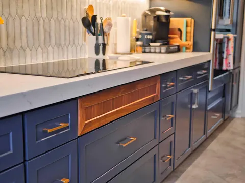 White quartz countertop over navy drawers with brass pulls and a walnut accent panel