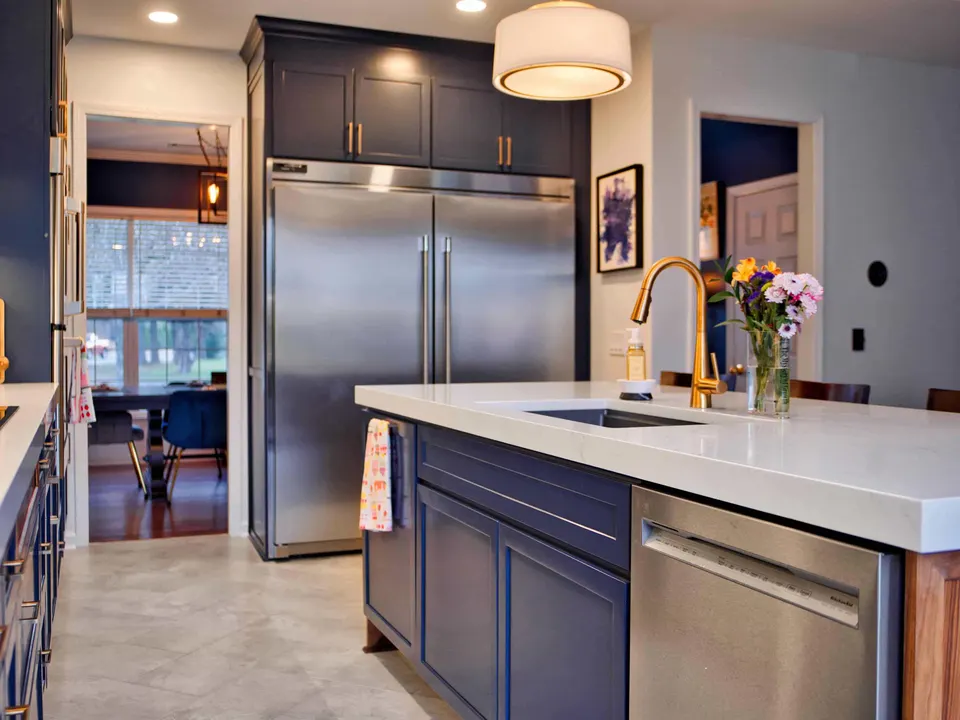 Navy island with a white quartz top and brass faucet, with a stainless refrigerator beyond