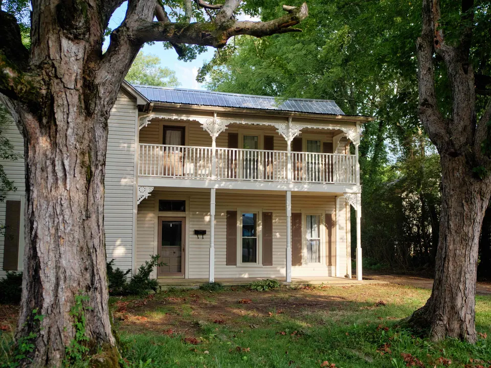 Two-story farmhouse with a restored double porch, white spindle railings and Victorian brackets