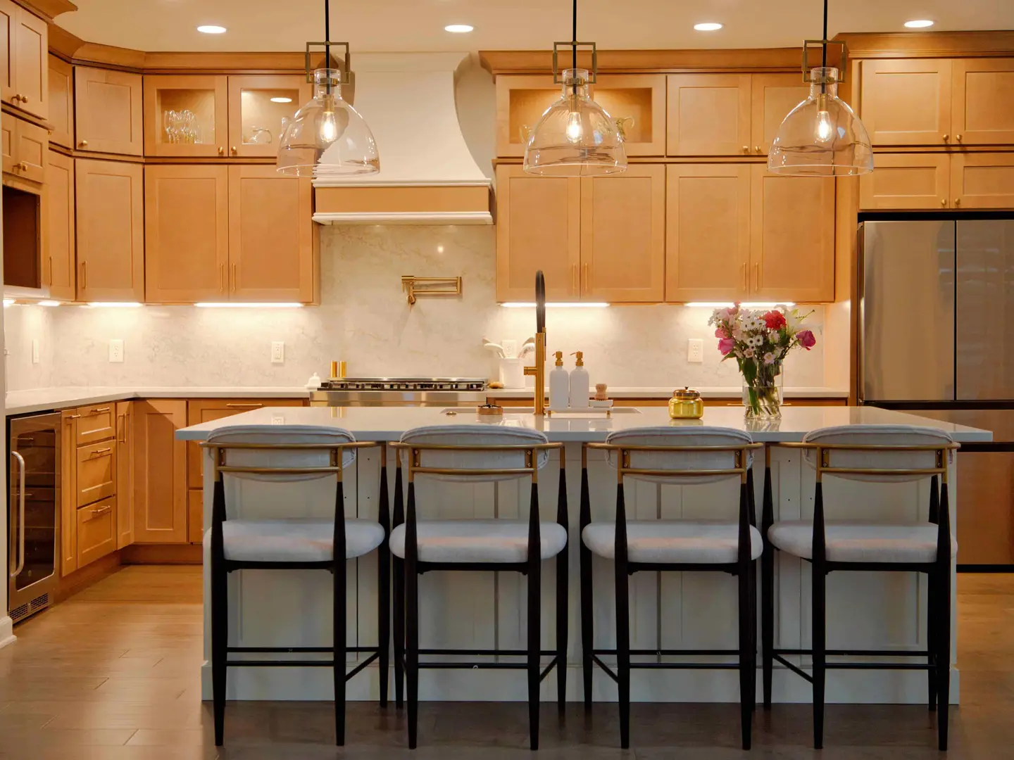 Kitchen with natural maple shaker cabinets, a white plaster range hood, glass pendants and island seating for four