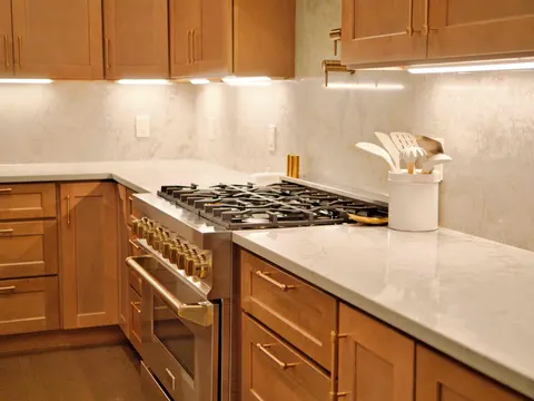 Professional gas range with brass knobs between maple cabinets and quartz countertops