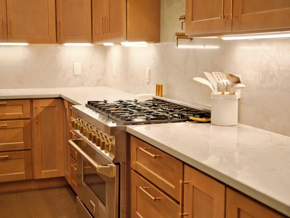 Professional gas range with brass knobs between maple cabinets and quartz countertops