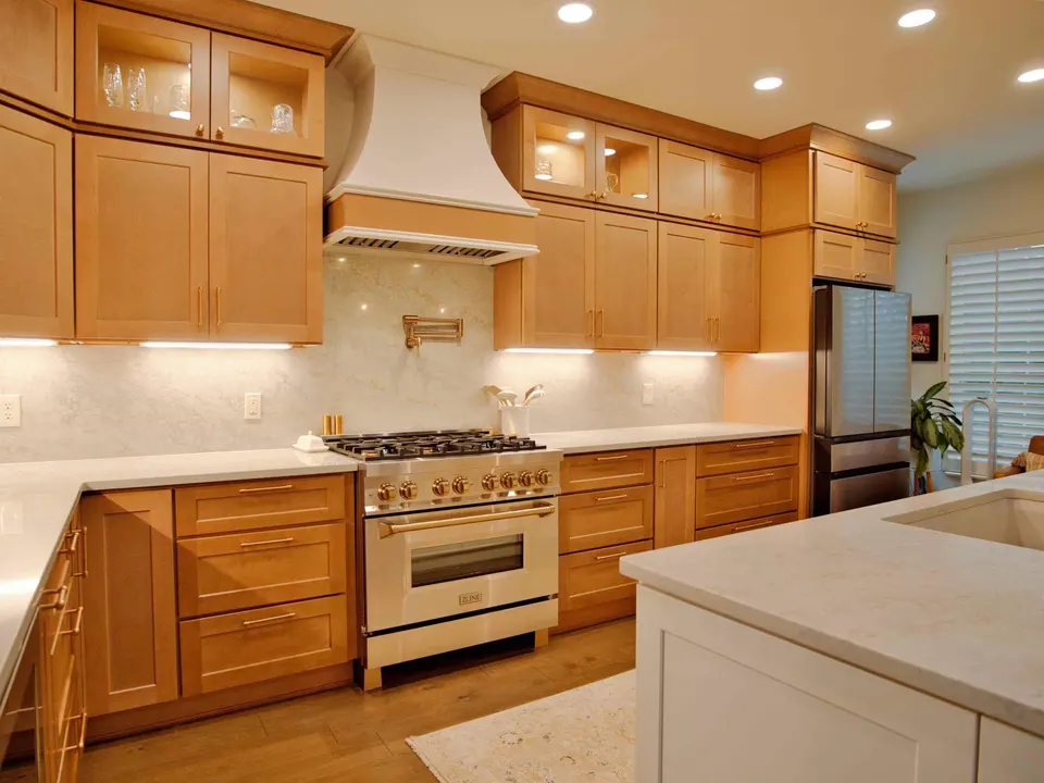 Range wall with a white plaster hood, pot filler and lit glass-front maple cabinets