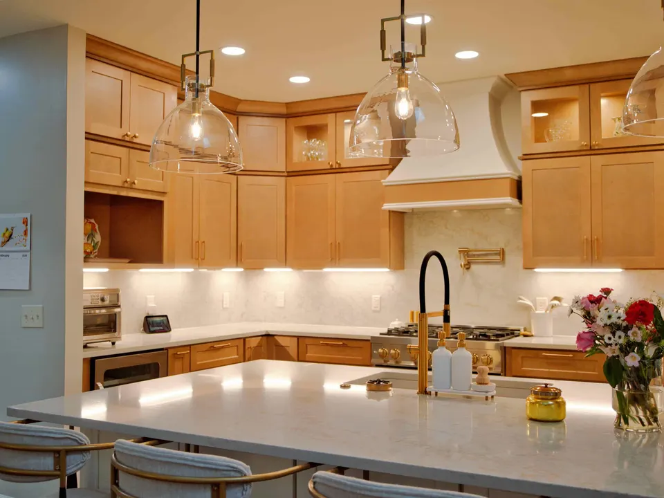 Island with a brass pull-down faucet under glass pendants, facing a maple kitchen