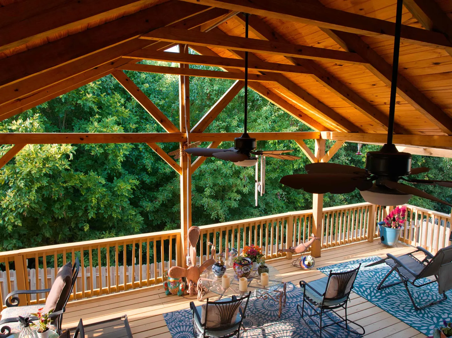 Timber-frame covered deck with a vaulted pine ceiling, ceiling fans and wood railings overlooking the trees