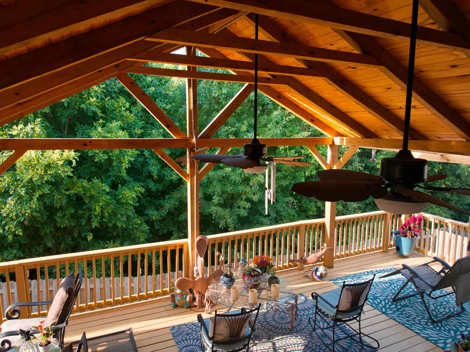 Timber-frame covered deck with a vaulted pine ceiling, ceiling fans and wood railings overlooking the trees