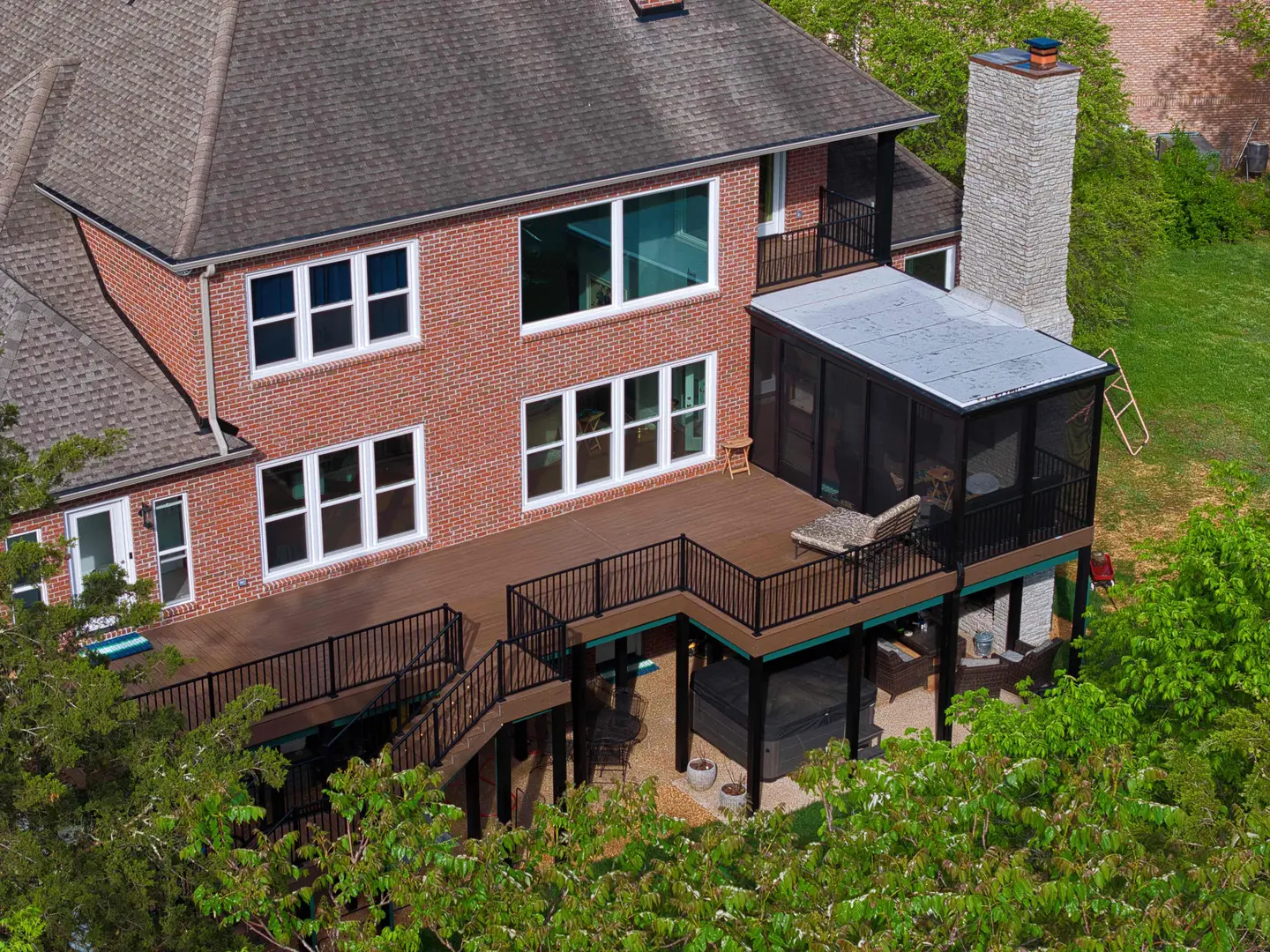 Aerial view of a brick home with a multi-level composite deck, black railings and a screened porch