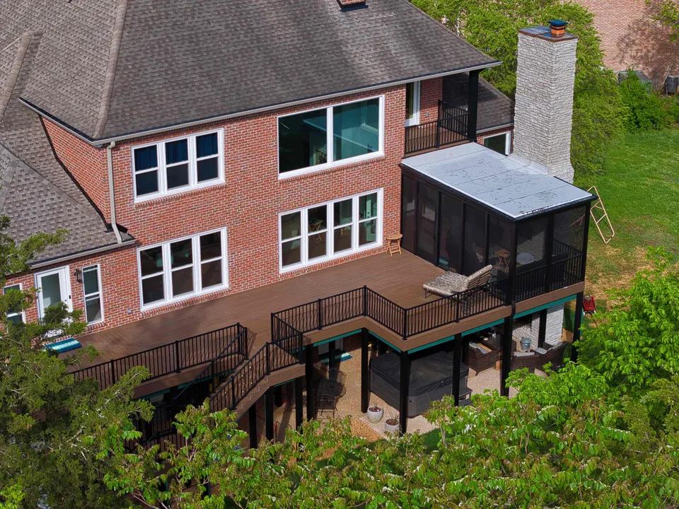 Aerial view of a brick home with a multi-level composite deck, black railings and a screened porch