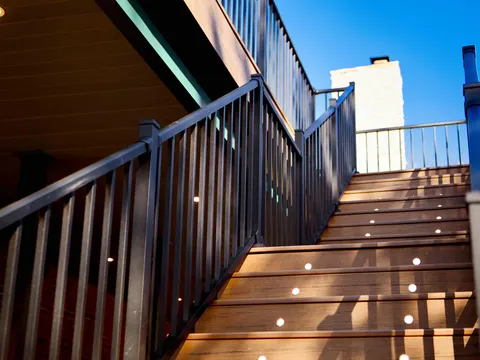 Composite deck stairs with built-in step lights and black railings beside a painted brick chimney