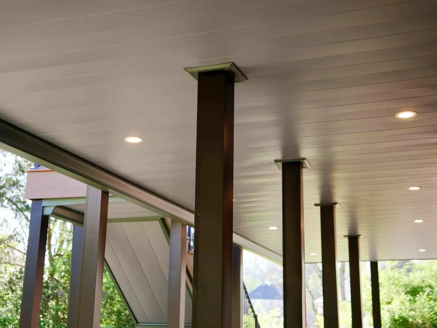 Covered patio beneath an upper deck with a finished ceiling, recessed lighting and black posts