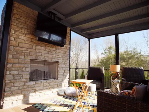 Covered porch with a stacked-stone fireplace, mounted TV and lounge seating