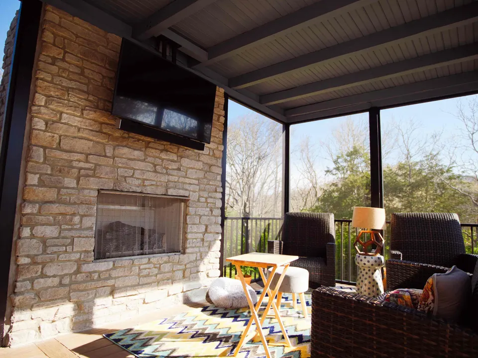 Covered porch with a stacked-stone fireplace, mounted TV and lounge seating