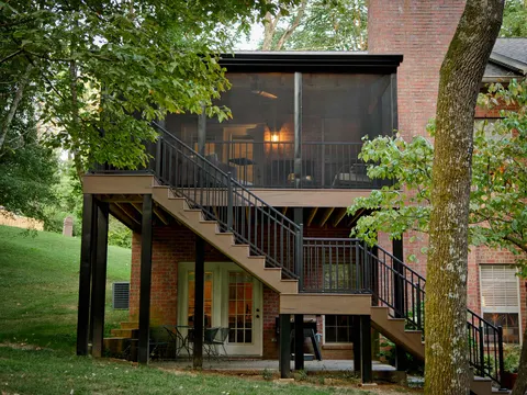 Elevated screened porch with a composite staircase on the back of a brick home