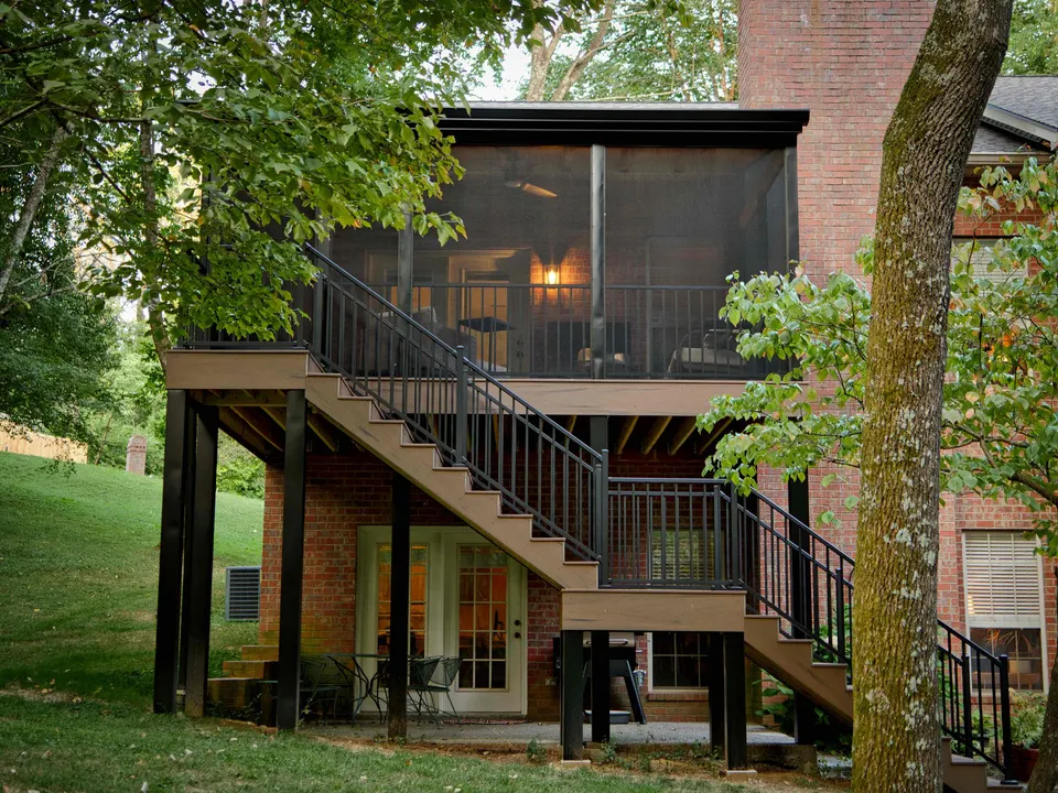 Elevated screened porch with a composite staircase on the back of a brick home