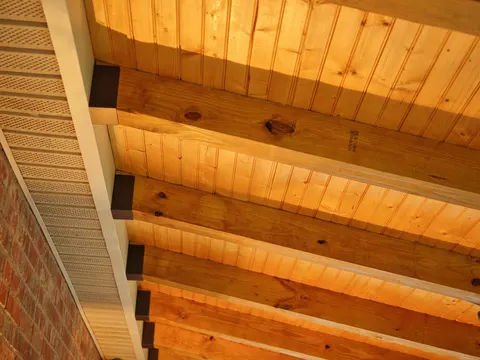 Exposed rafters and a tongue-and-groove ceiling meeting a brick wall
