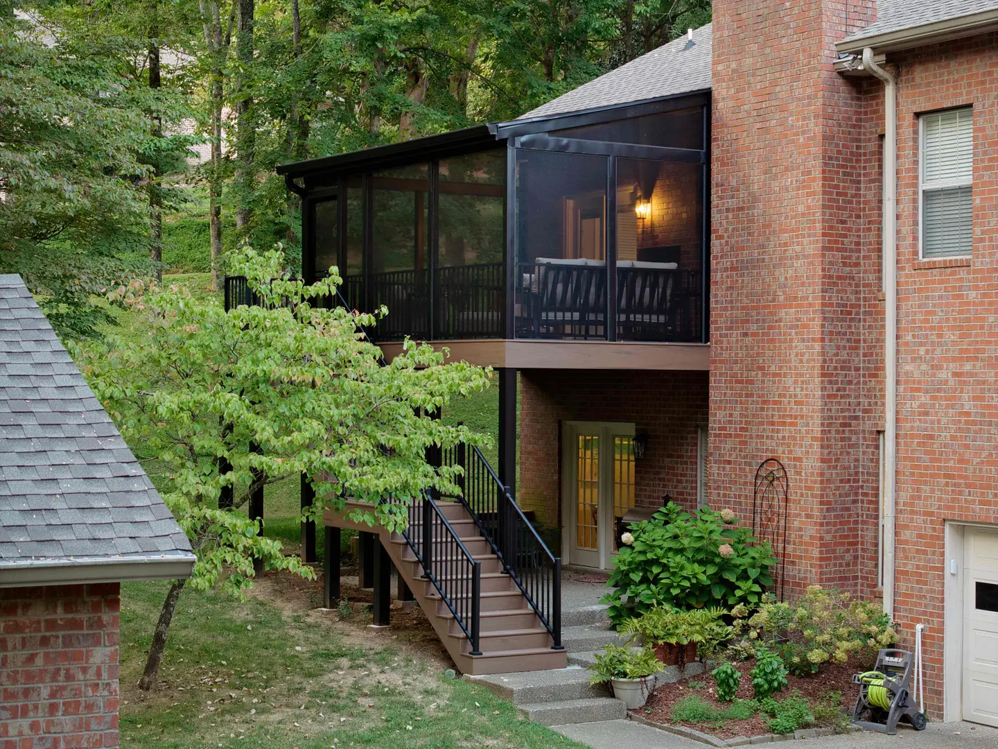 Screened porch addition with stairs on the side of a two-story brick home