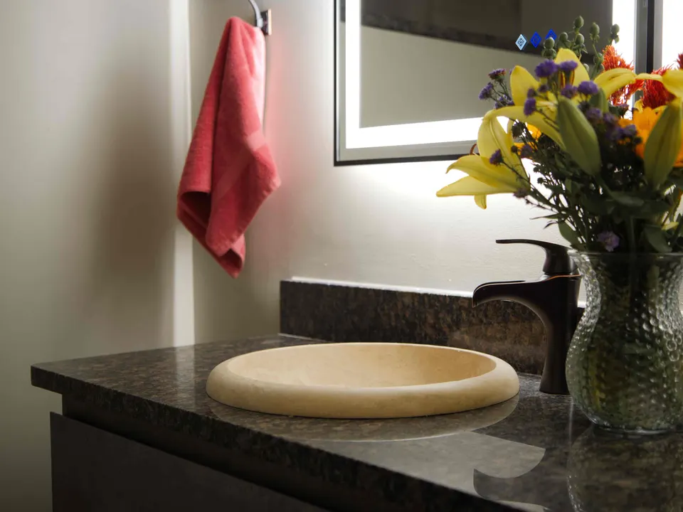 Stone vessel sink on a dark granite vanity top with an oil-rubbed bronze faucet and backlit mirror