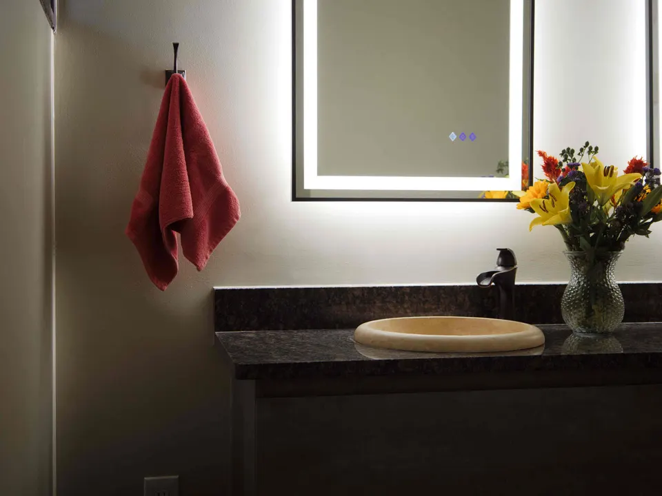 Floating vanity with a dark granite top, stone vessel sink and backlit mirror