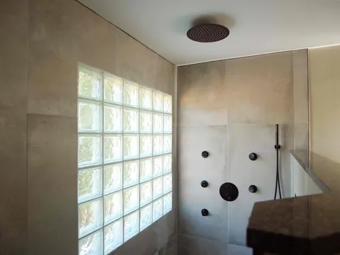 Walk-in shower in large-format tile with a glass-block window, ceiling rain head and matte black body sprays