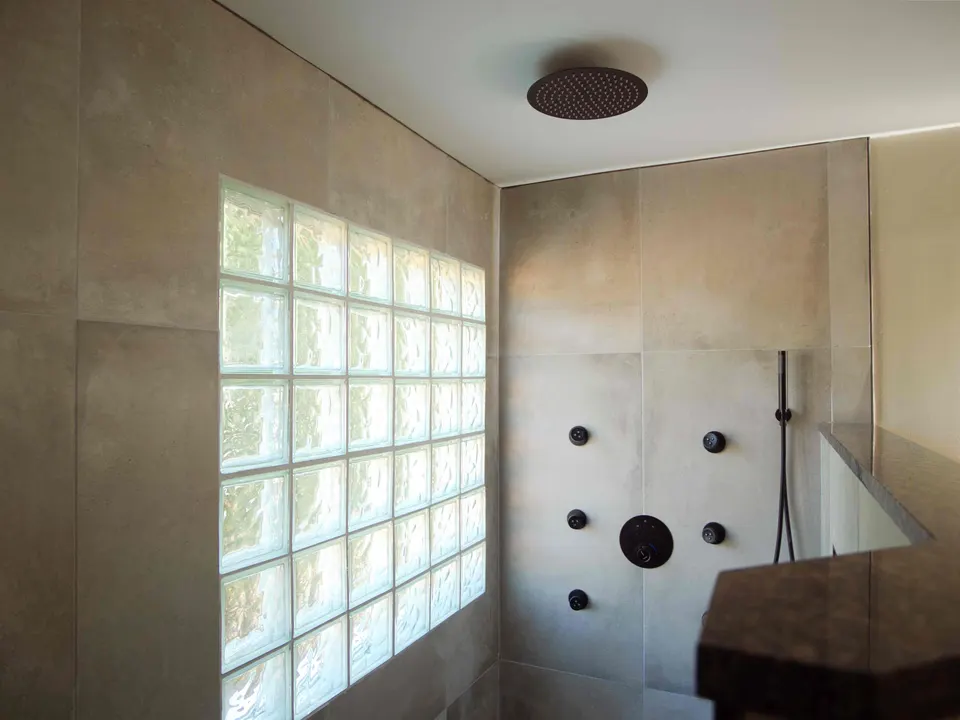Walk-in shower in large-format tile with a glass-block window, ceiling rain head and matte black body sprays