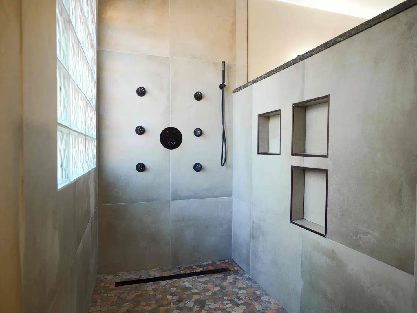 Large-format tile shower with six body sprays, a linear drain, pebble floor and three recessed niches