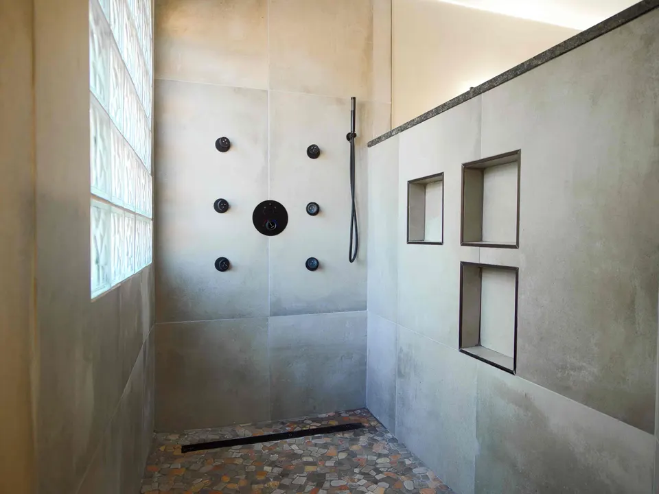 Large-format tile shower with six body sprays, a linear drain, pebble floor and three recessed niches