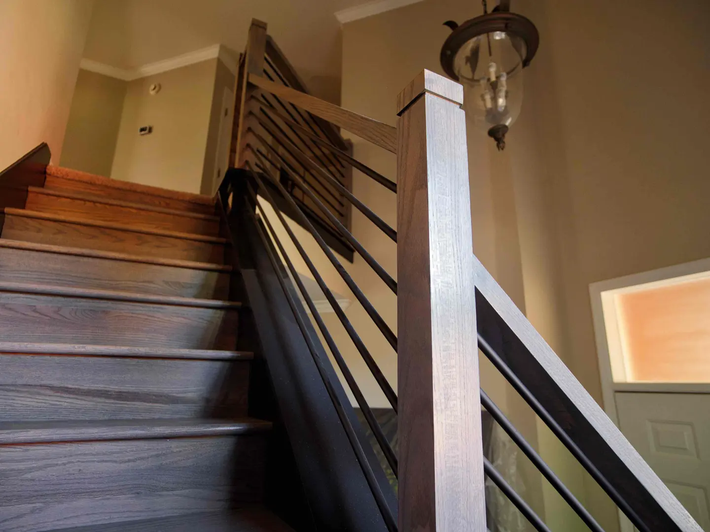 Stained wood stair treads with a horizontal metal railing and lantern pendant