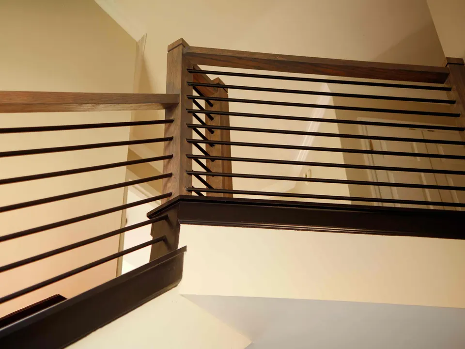 Stair landing with a stained wood handrail and horizontal black balusters