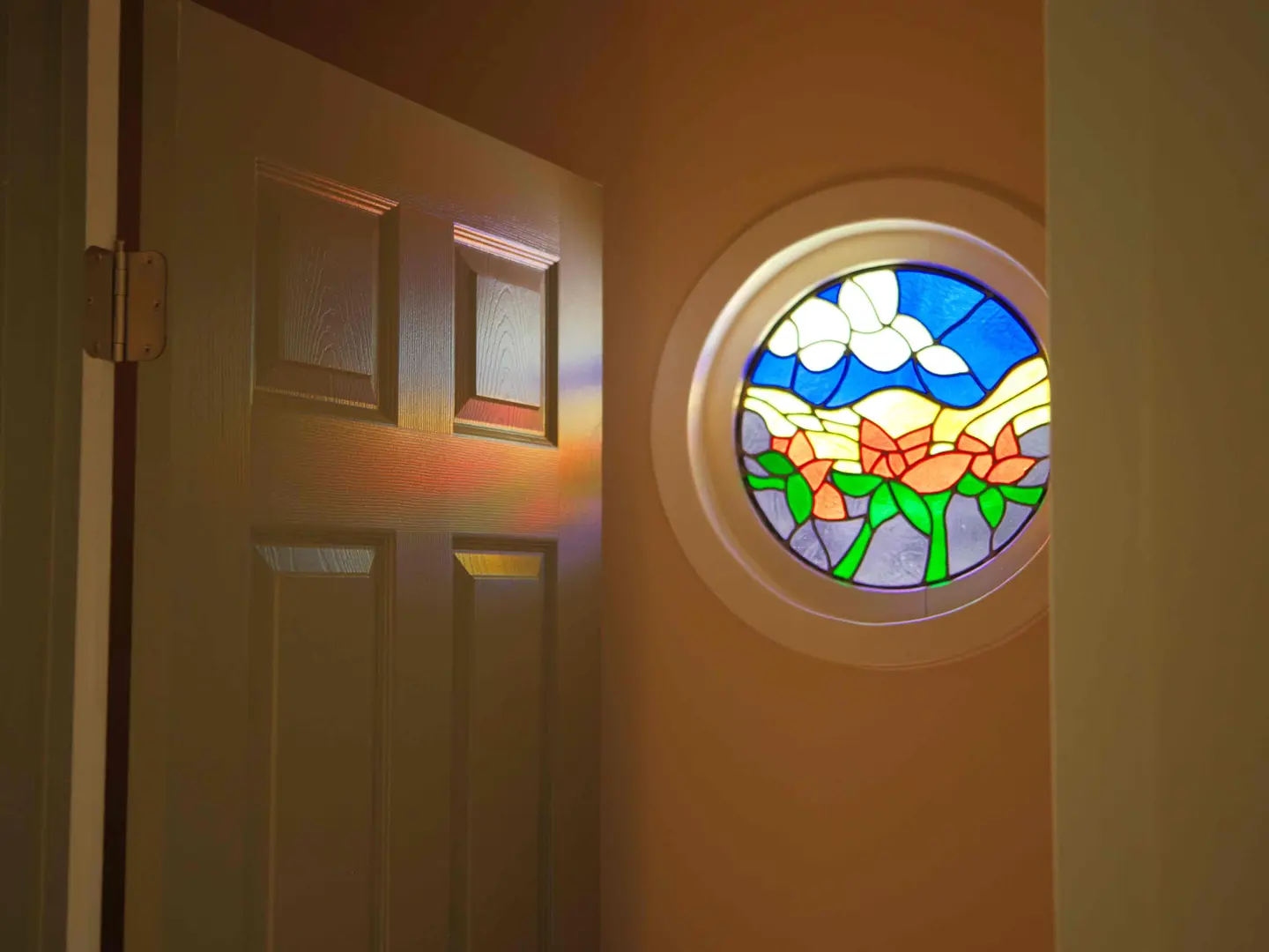 Round stained-glass window with a floral design beside a six-panel door