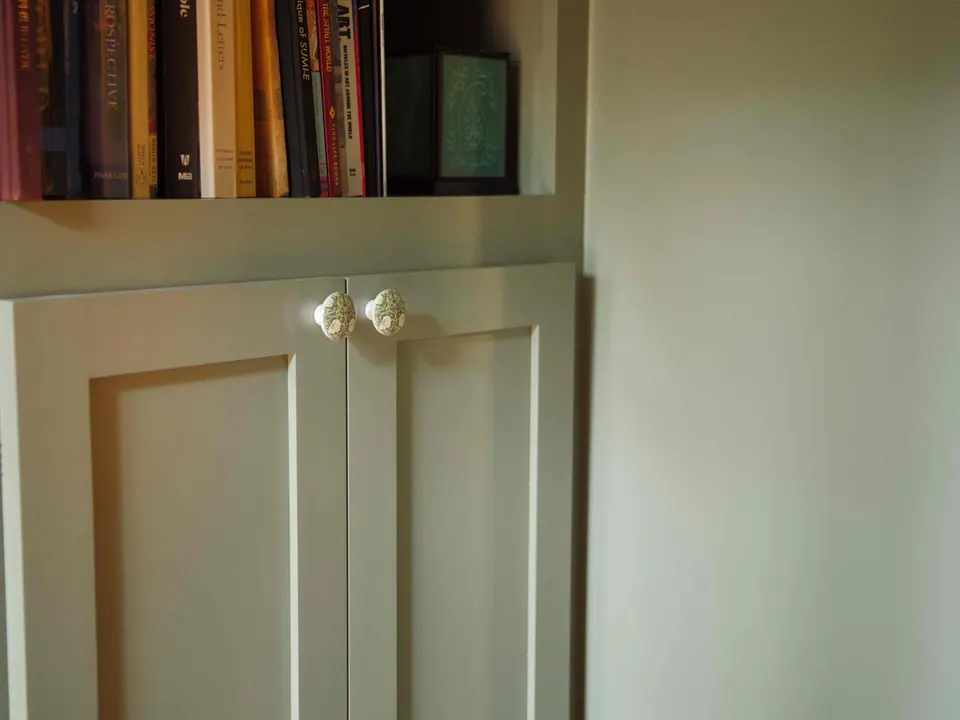 Sage green built-in cabinet with a bookshelf above