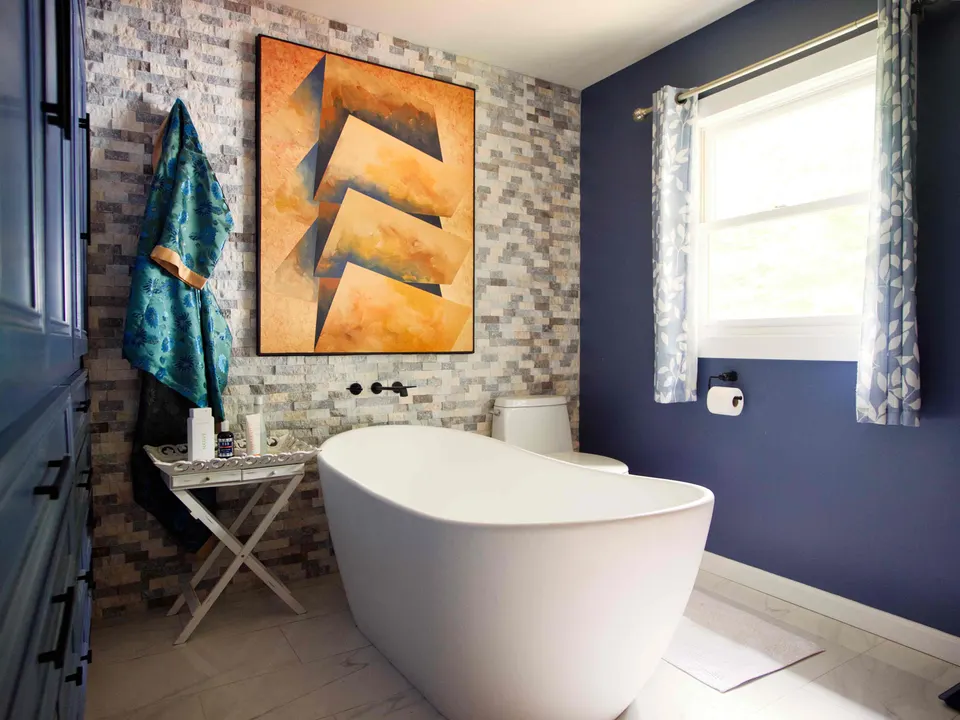 Freestanding soaking tub against a stacked-stone accent wall with a wall-mounted filler and navy walls