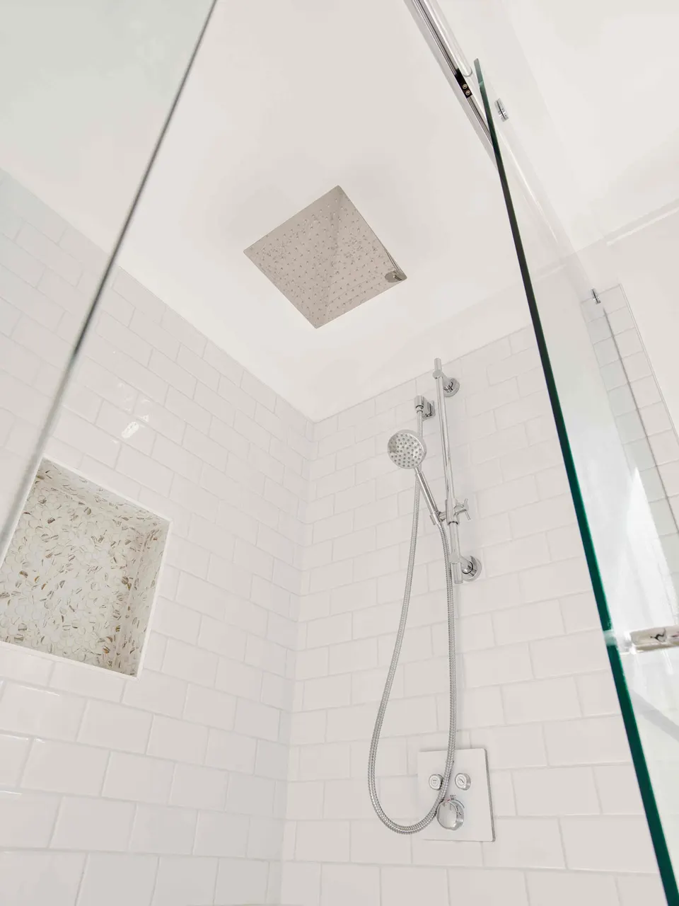 Walk-in shower with white subway tile, a ceiling rain head, slide-bar hand shower and mosaic niche behind frameless glass