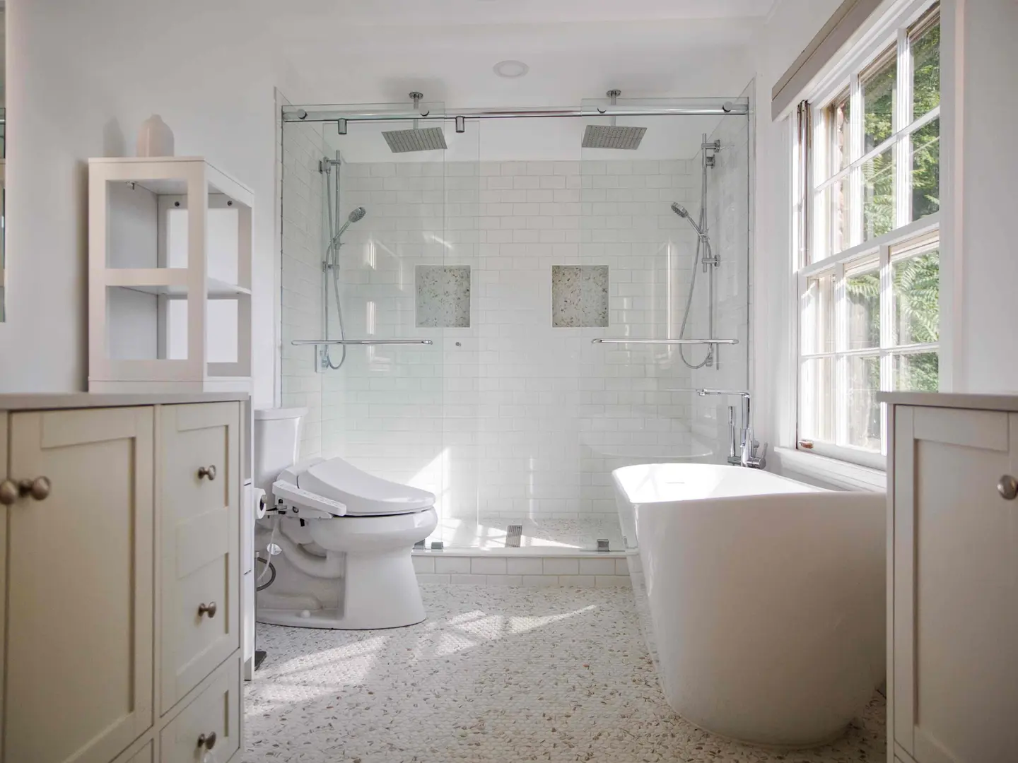 Two-person glass shower with twin rain heads between a freestanding soaking tub and paired white vanities