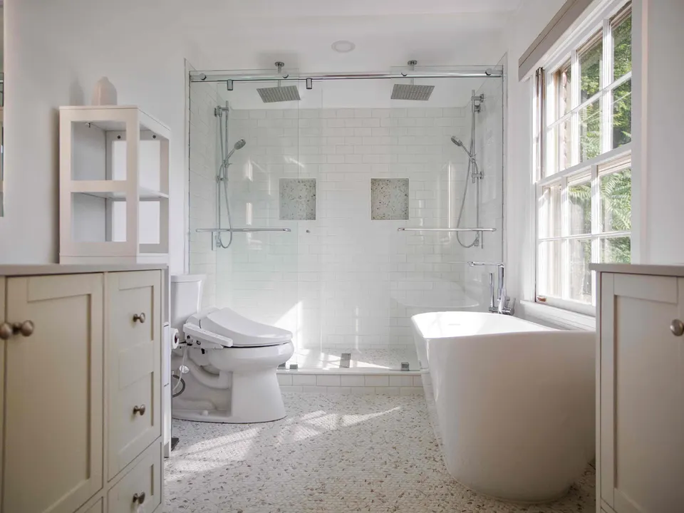 Two-person glass shower with twin rain heads between a freestanding soaking tub and paired white vanities