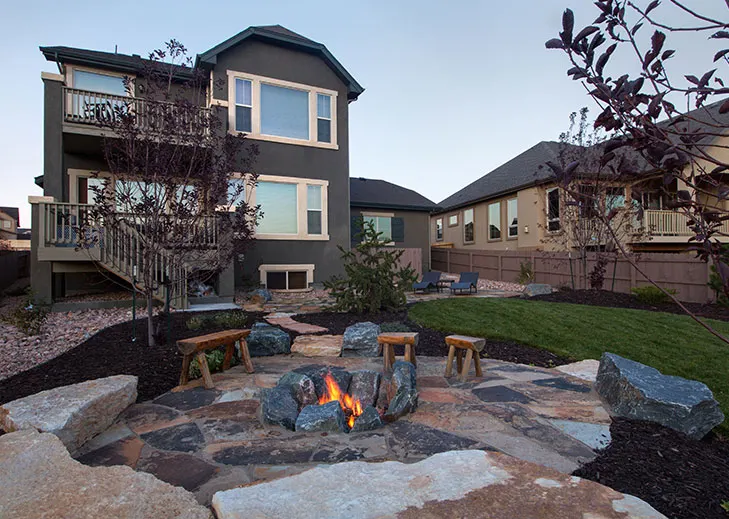 Flagstone patio with a stone fire pit and boulder seating in a backyard