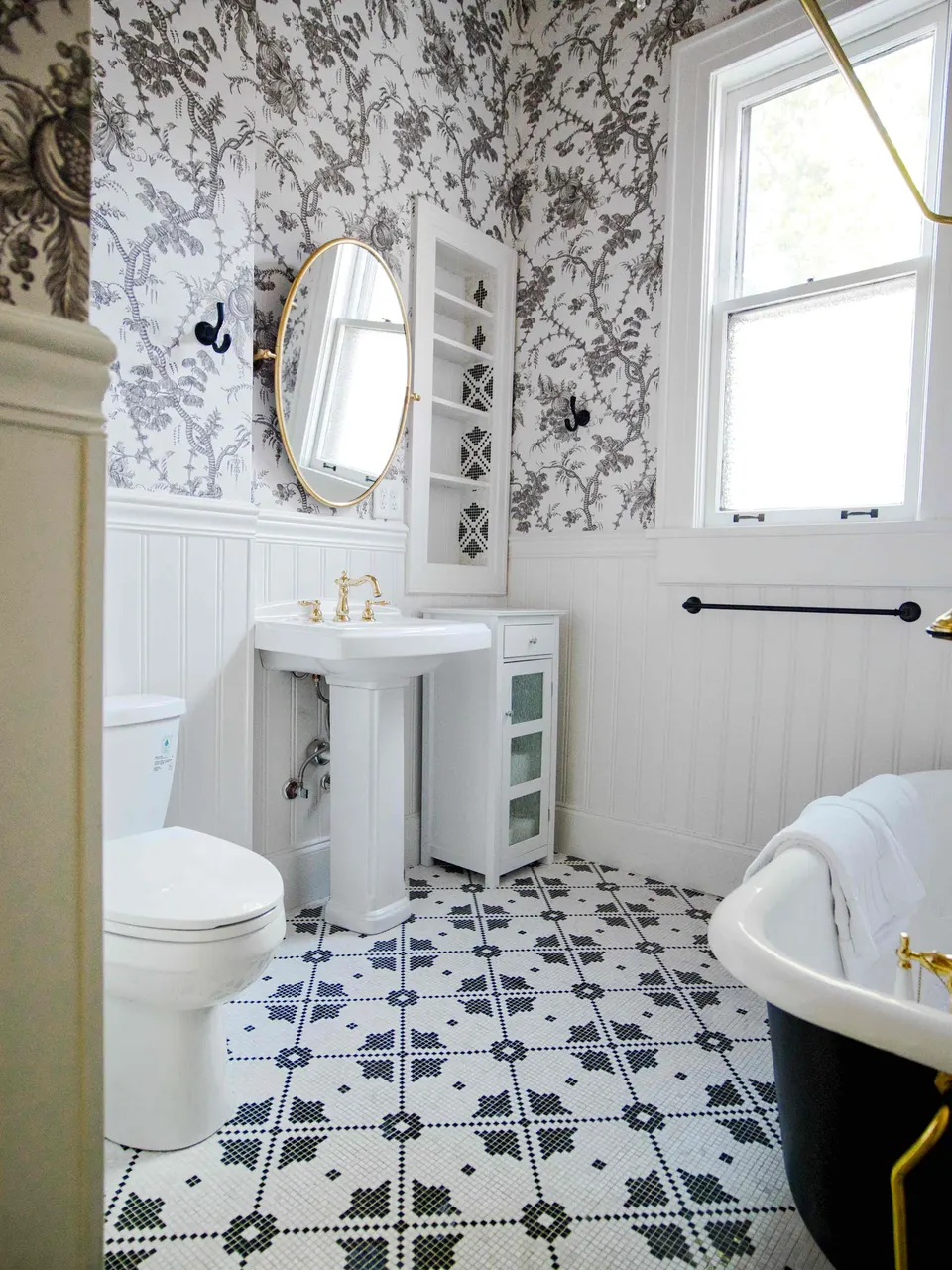 Bathroom with black-and-white botanical wallpaper, beadboard wainscoting, a pedestal sink, mosaic tile floor and clawfoot tub