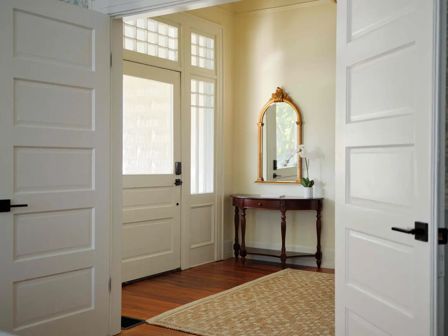 Entry hall with five-panel doors, a glass-paneled front door with transom, hardwood floors and a gilded mirror