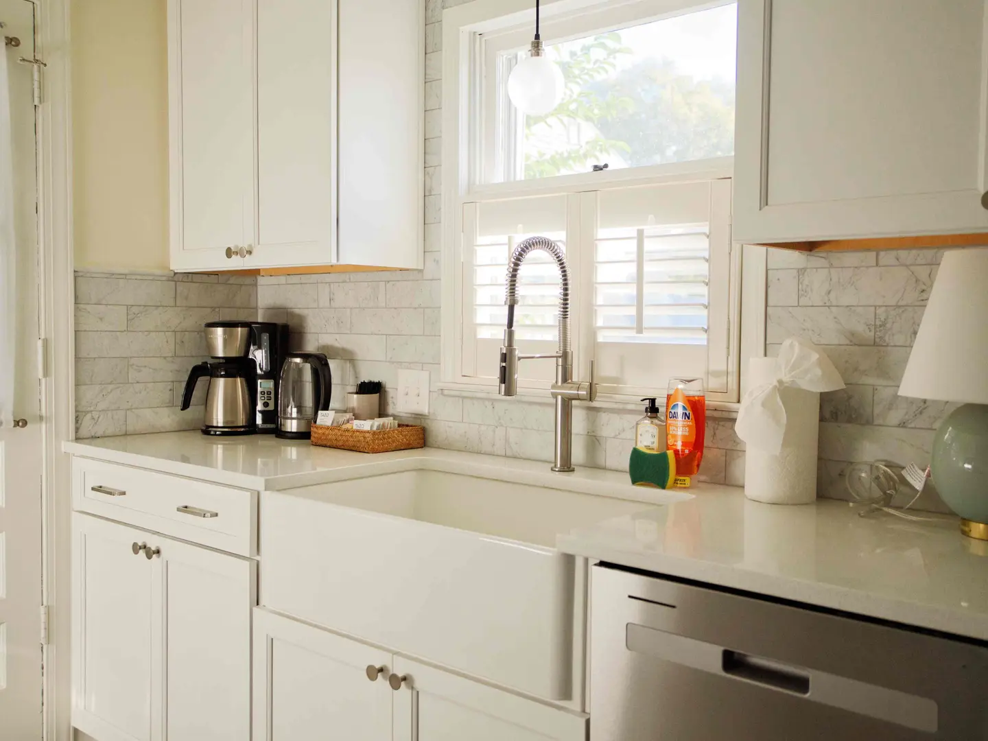 White shaker kitchen with a farmhouse sink, marble subway tile and plantation shutters