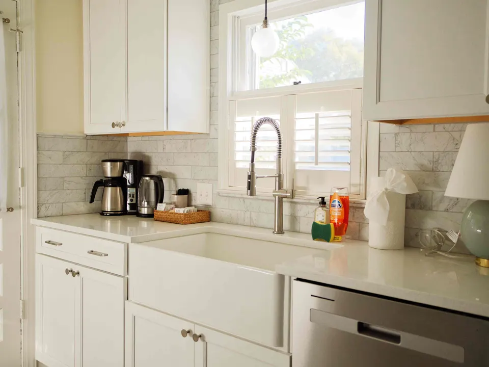 White shaker kitchen with a farmhouse sink, marble subway tile and plantation shutters