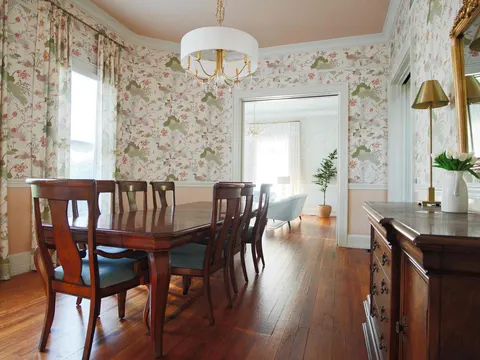Dining room with botanical wallpaper, a chair rail, drum chandelier and wide-plank hardwood floors