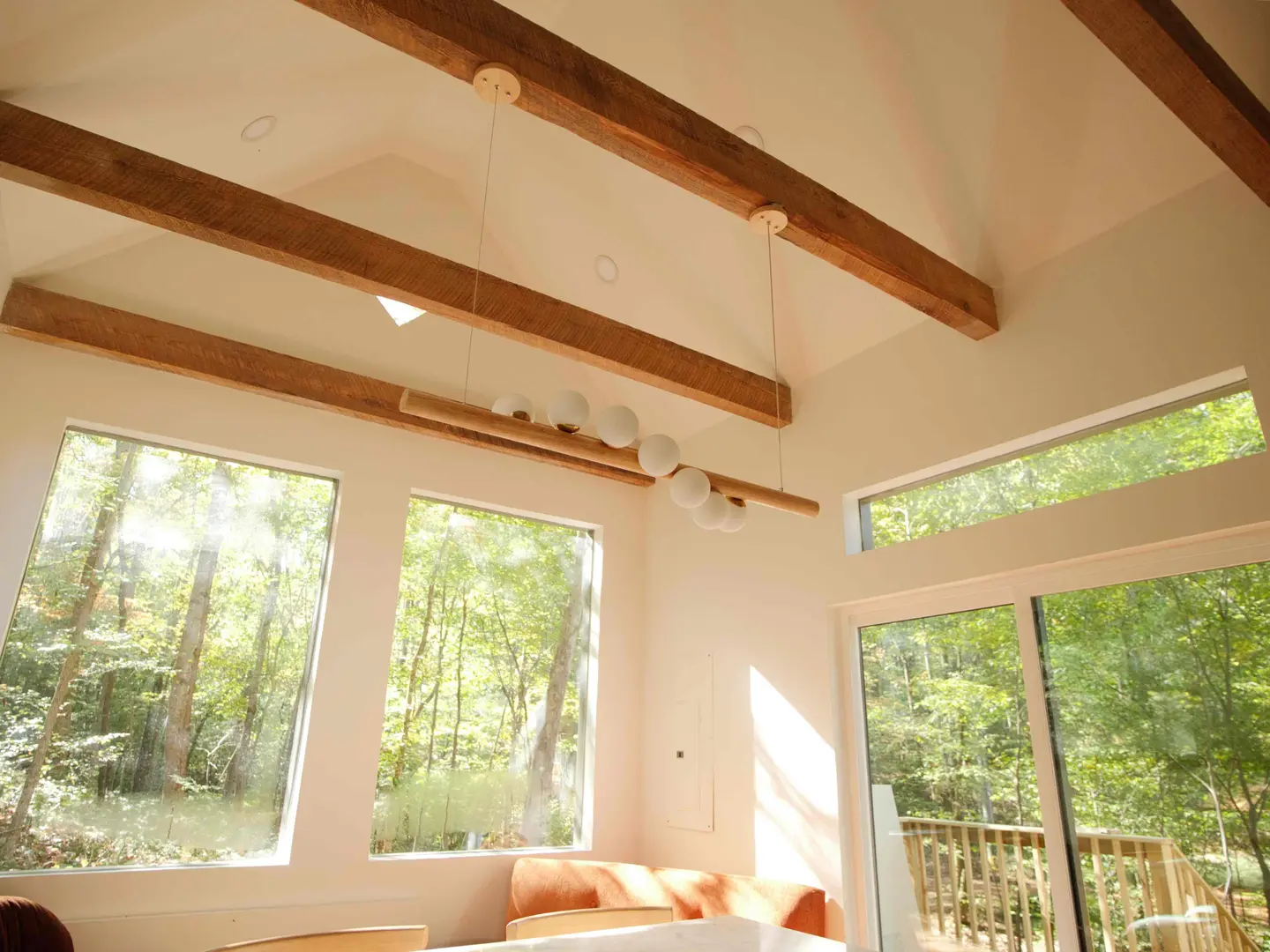 Vaulted cabin living room with reclaimed timber beams, a globe pendant and tall windows onto the woods
