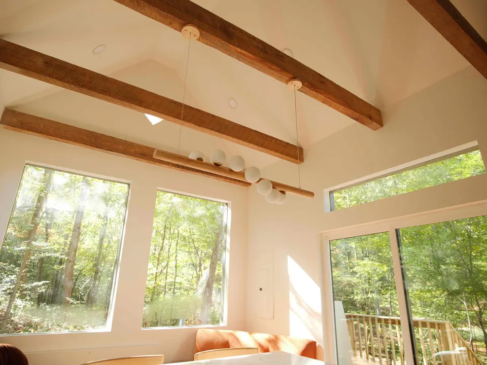 Vaulted cabin living room with reclaimed timber beams, a globe pendant and tall windows onto the woods