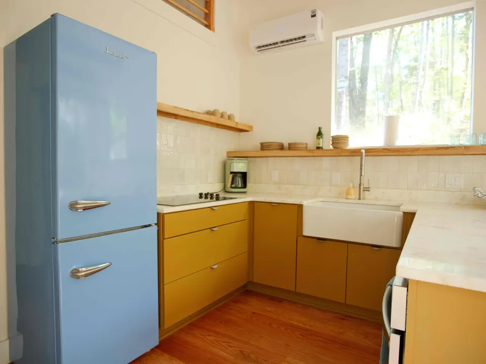 Cabin kitchen with ochre cabinets, a farmhouse sink, glazed tile, open wood shelves and a pale blue retro refrigerator