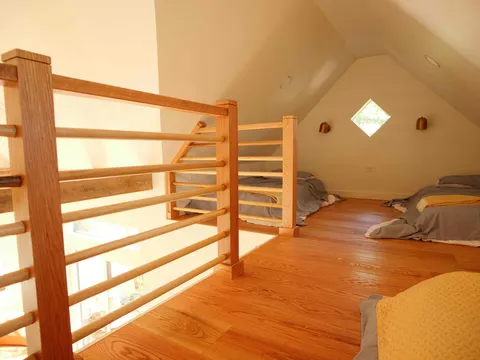Sleeping loft with a handcrafted wood railing, hardwood floors and a diamond window