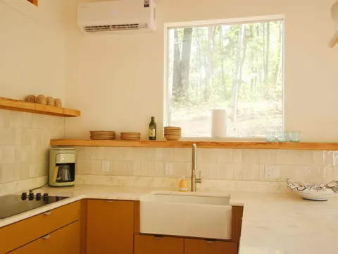 Cabin kitchen corner with a ductless mini-split, cooktop, farmhouse sink, glazed tile and live-edge wood shelf